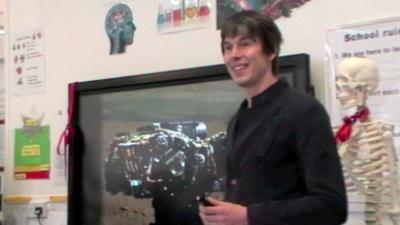 Brian Cox talks in classroom in front of AV screen