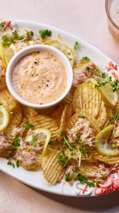 Crab loaded crisps on an oval shaped plate, with a round container of sauce in the middle