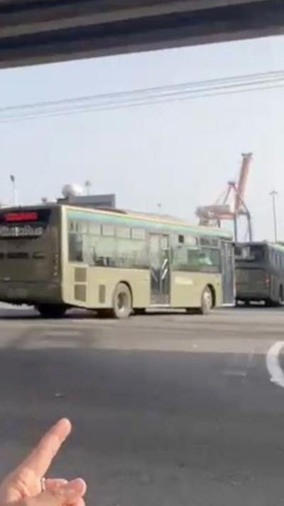 A hand pointing at military buses driving down a road