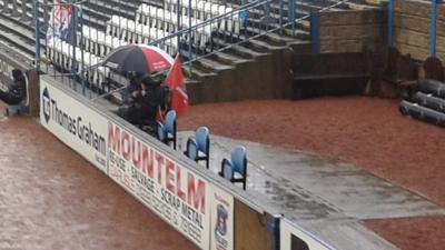 Jordan and his dad watching football under an umbrella at Brunton Park