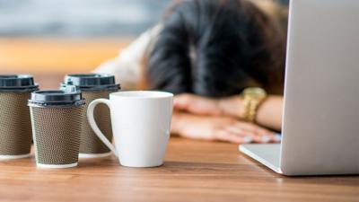 A woman with her head down with a laptop and coffee cups