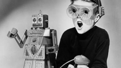 Black and white image of child wearing retro futuristic glasses alongside a retro robot