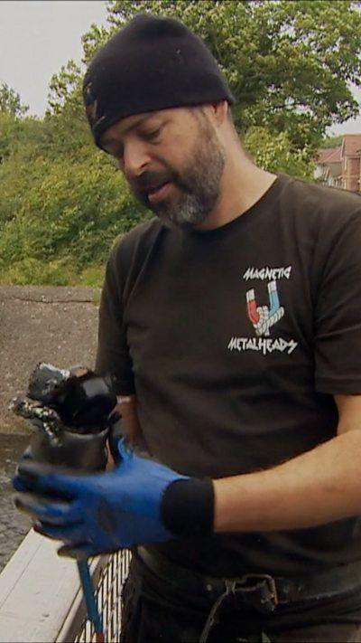 A man wearing a beanie hat and black t-shirt is holding a magnet