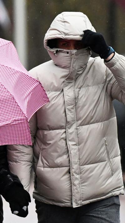 A person in a winter coat clutching their hood in strong wind