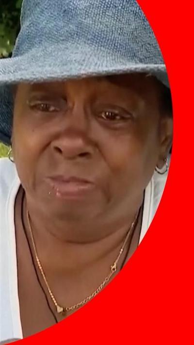 Adrienne Jones-McAllister, wearing a dark sun hat and white shirt, getting emotional in an interview.