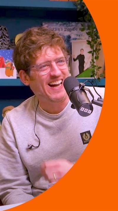A man, Elis James, smiles in front of a microphone.
