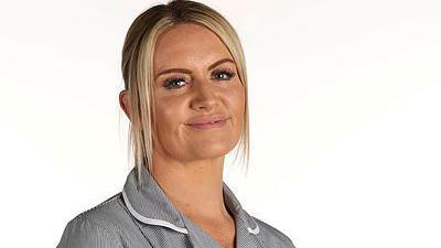 A woman with blonde hair in a nurse's outfit smiling 