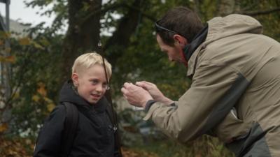 Fisherman Kieron Banks prepares a rod and a line while a young boy, who has blonde hair, looks at the hook.