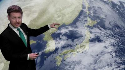 Tomasz Schafernaker standing in front of a satellite image of cloud over Japan