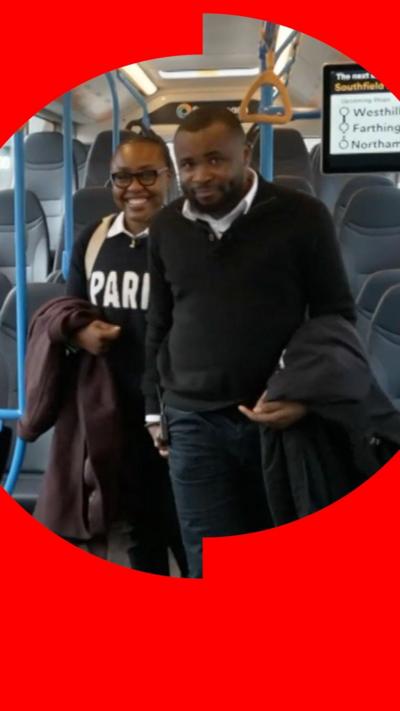 A man and a woman smile while walking through a bus