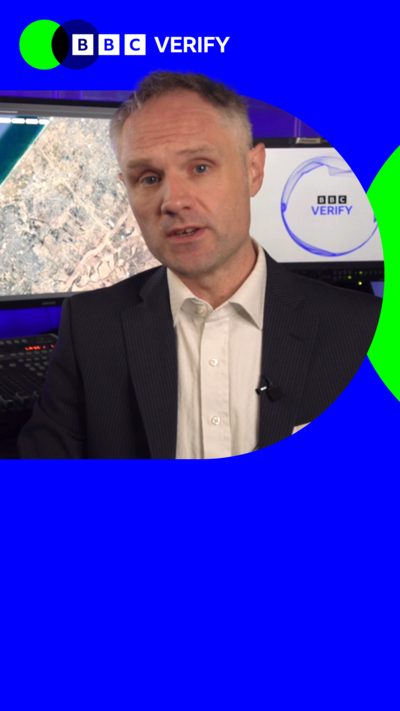 BBC Verify journalist Richard Irvine-Brown reporting. He is pictured before two monitors, one of which is showing the BBC Verify logo. The image is imposed over the BBC Verify colours and branding. 