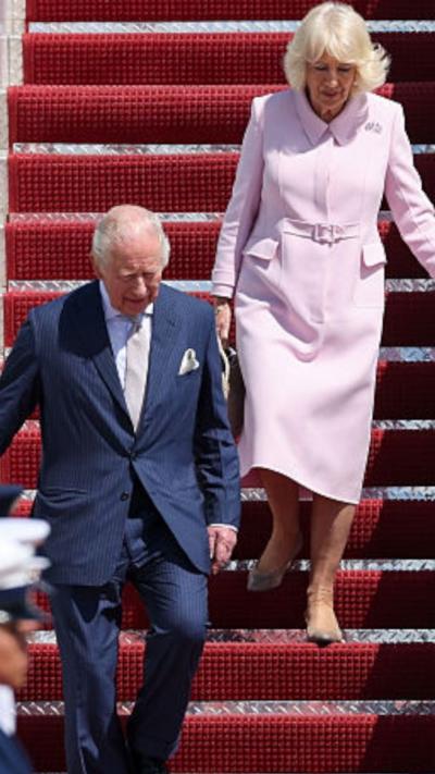 King Charles and Queen Camilla come down the staircase off a plane.