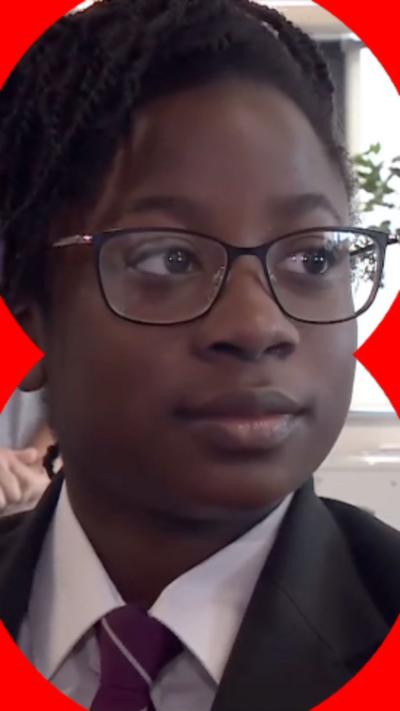 Student in uniform looking at a reporter holding a mic to her.