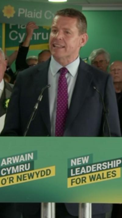 Rhun ap Iorwerth stood at a podium making a speech