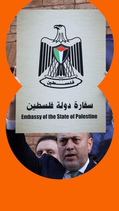 A man holds a sign with an image of a bird with Palestinian flag colours, with the words Embassy of the State of Palestine. 