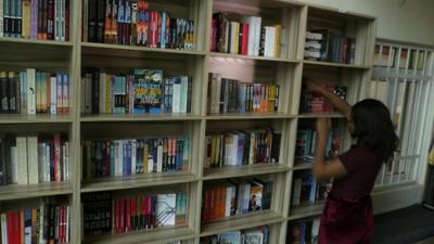 A woman putting a book into a bookshelf