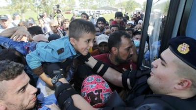A policeman helps a boy as people board a bus in Croatia