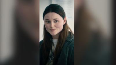 A young woman with long dark hair smiles to someone off screen.