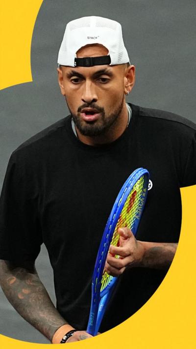 Nick Kyrgios. He is holding a tennis racquet, and is wearing a black shirt and a white cap.