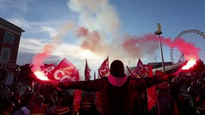 A protester in France holds red flares in front of a crowd of people.