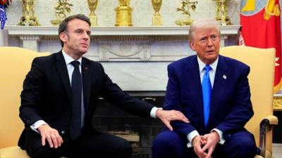 Emmanuel Macron holding Donald Trump's arm while seated beside each other in the Oval Office