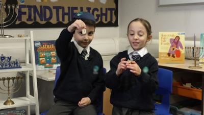 Two young children in school uniform hold up dreidels