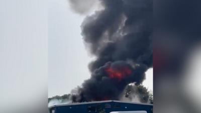 Video shows a large, black plume of smoke and flames rising from the site of a fire at a commercial building..