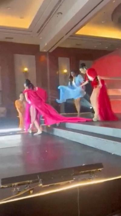 Women in evening dresses walk off of a stage.
