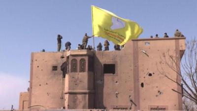 Kurdish-led fighters in eastern Syria raise a yellow flag as they celebrate the defeat of IS