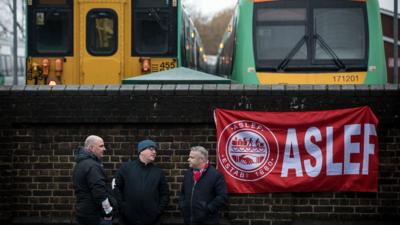 Men and an ASLEF flag on the wall near trains