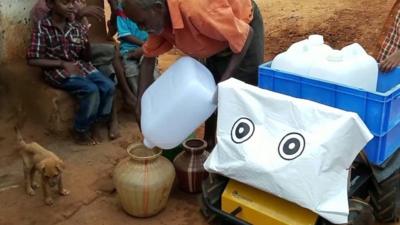 A water carrying robot stands next to a man pouring water