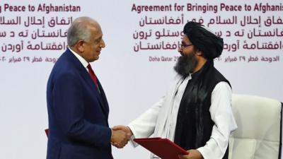 Zalmay Khalilzad and Taliban co-founder Mullah Abdul Ghani Baradar shake hands