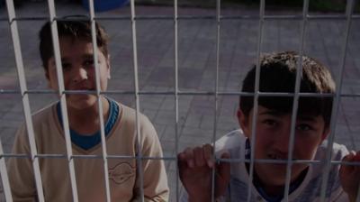 Children looking through a wire fence at the camera