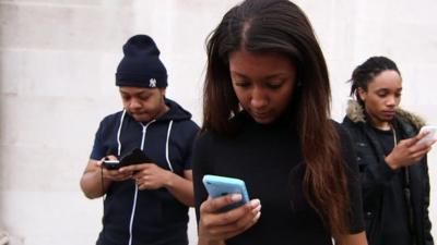 Three black British teenagers looking down at the smartphones they are holding