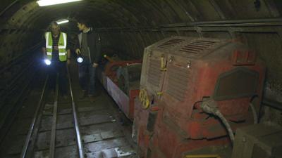 Ray Middlesworth (L) and Henry Golding (R) stand next to a 'Mail Rail' train