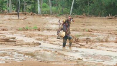 man carrying possessions through mud