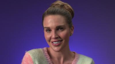 Danielle Lloyd smiles wearing a multicoloured cardigan; she has brown hair tied in a bun
