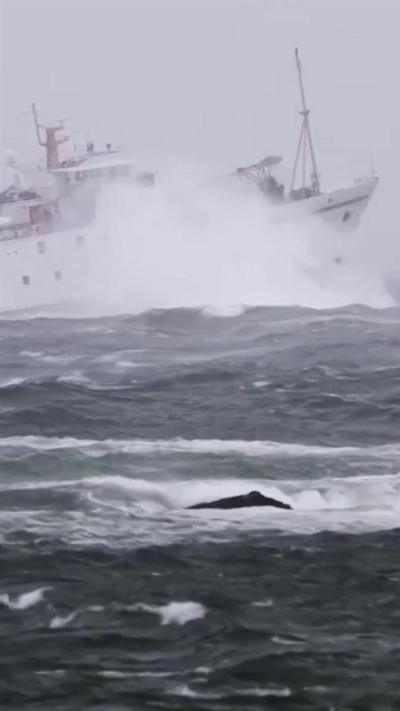 A white boat on the sea. There are large waves. The sky is grey. 