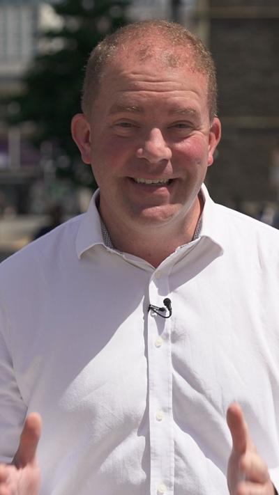 A man in a white shirt, with short hair is looking at the camera