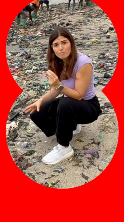 A woman crouching on a beach that is covered in textile rubbish