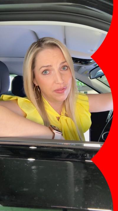 Presenter Emma Vardy looks out of the window from the driving seat of a car. She has long blonde hair and wears a yellow top