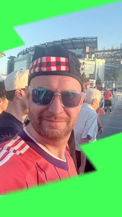 Man wears a Scotland top, hat and sunglasses, outside a sport stadium