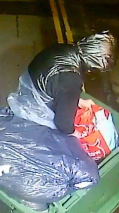 CCTV image of man wearing black hooded coat getting out of a commercial bin. 