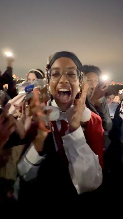 A young woman mid scream, with both hand close to her face, in a crowd of people.