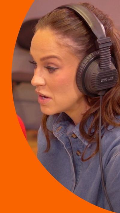 A woman with long, brown hair wears headphones and speaks into a microphone