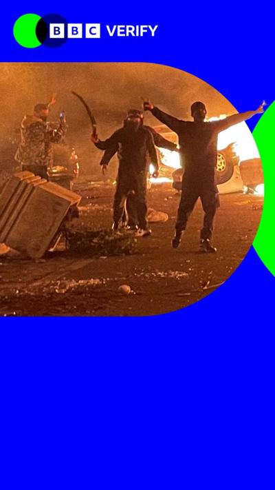 An image of Iranian Protesters gathering around burning cars while blocking a street during a protest in Tehran, Iran, on January 8, 2026. The image is outlined by BBC Verify branding which is blue.