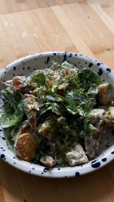 A while bowl with blue spots filled with a dressed potato and mackerel salad 