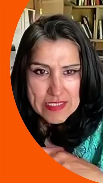 Dame Jasvinder Sanghera wears a blue outfit and sits facing the camera with bookshelves behind her