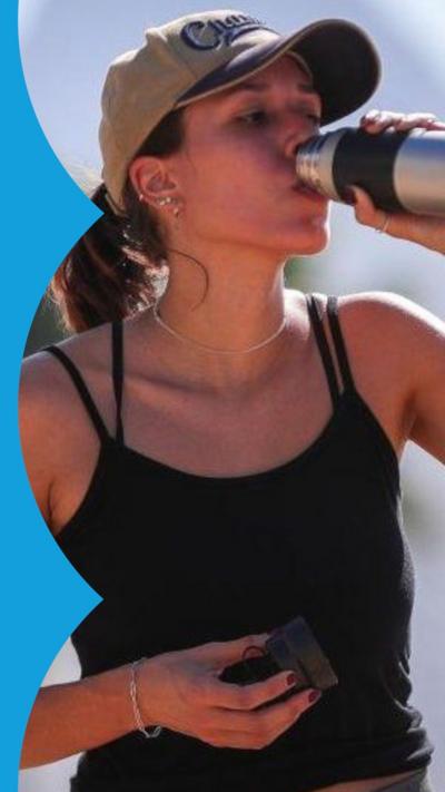 A woman with dark hair wearing a cap drinks from a bottle in the sun