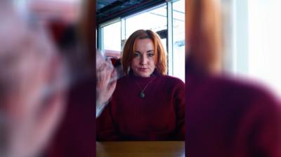 A woman frowns at the camera while a figure in a vampire cloak and makeup looms over her shoulder and into her face.